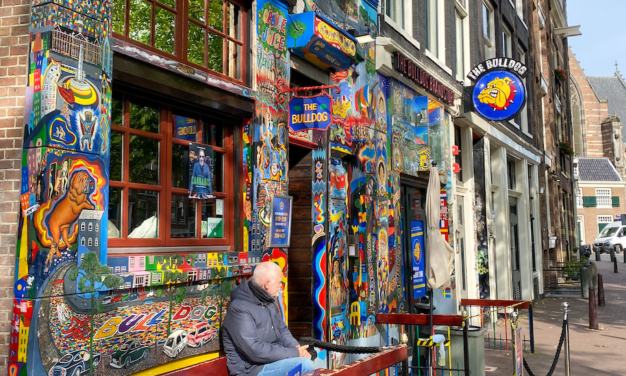 A man sits in front of the colourfully painted entrance to the Bulldog Coffeeshop, which the Amsterdamliebe red light tour also passes.